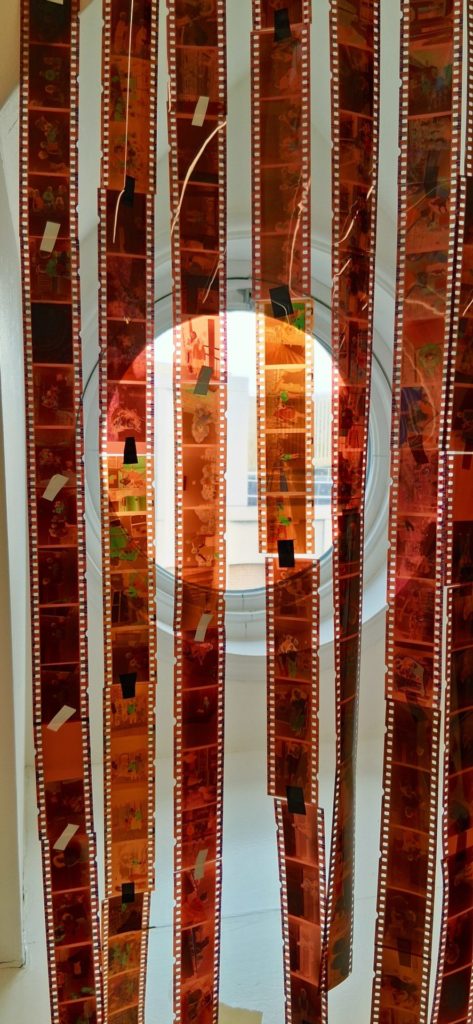 Strips of camera negatives are hung in front of a window.